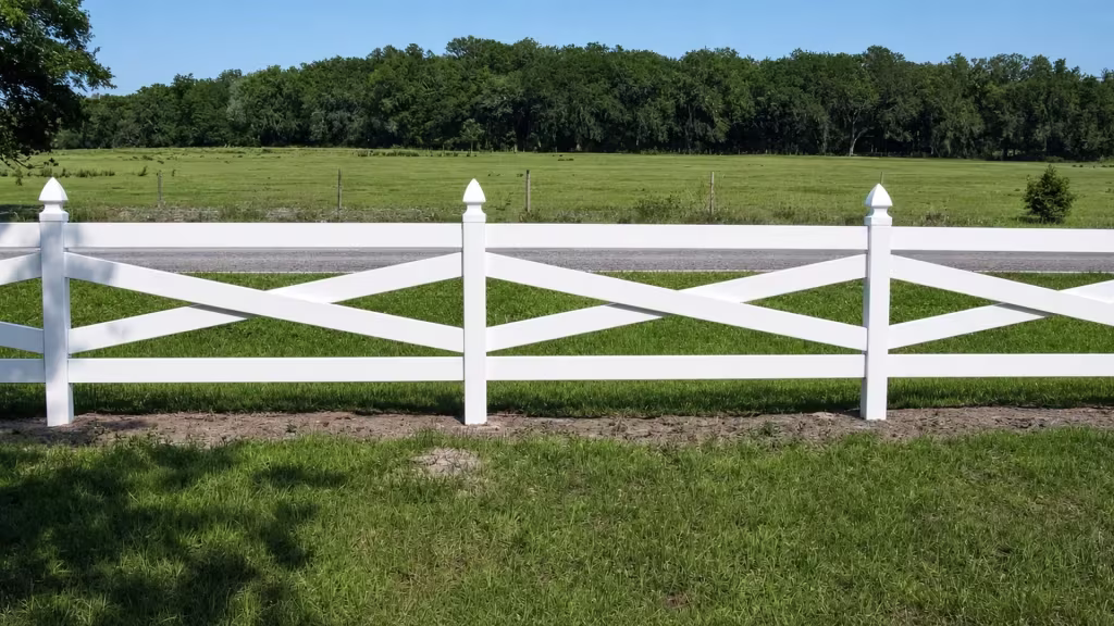 Distant wire fencing and a tree line border the pasture edge along this cross rail White vinyl run