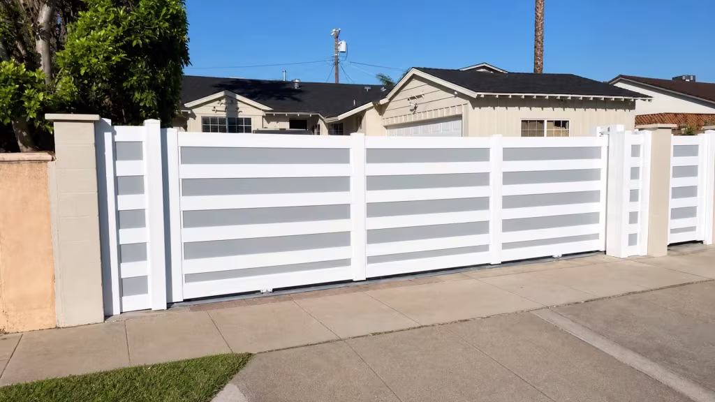 Pale frosted-acrylic bands run through this White vinyl rolling gate as it slides past a beige masonry column near the garage