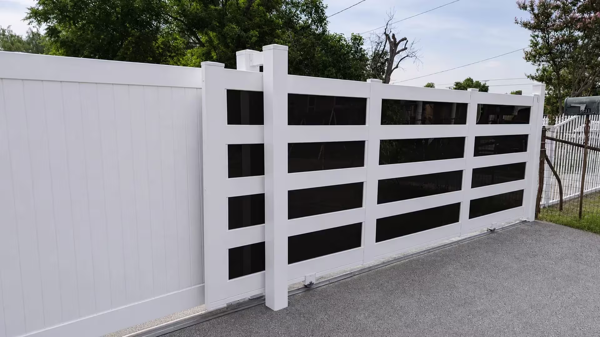 Four stacked dark acrylic openings fill each bay of this White vinyl rolling gate beside a solid privacy fence run