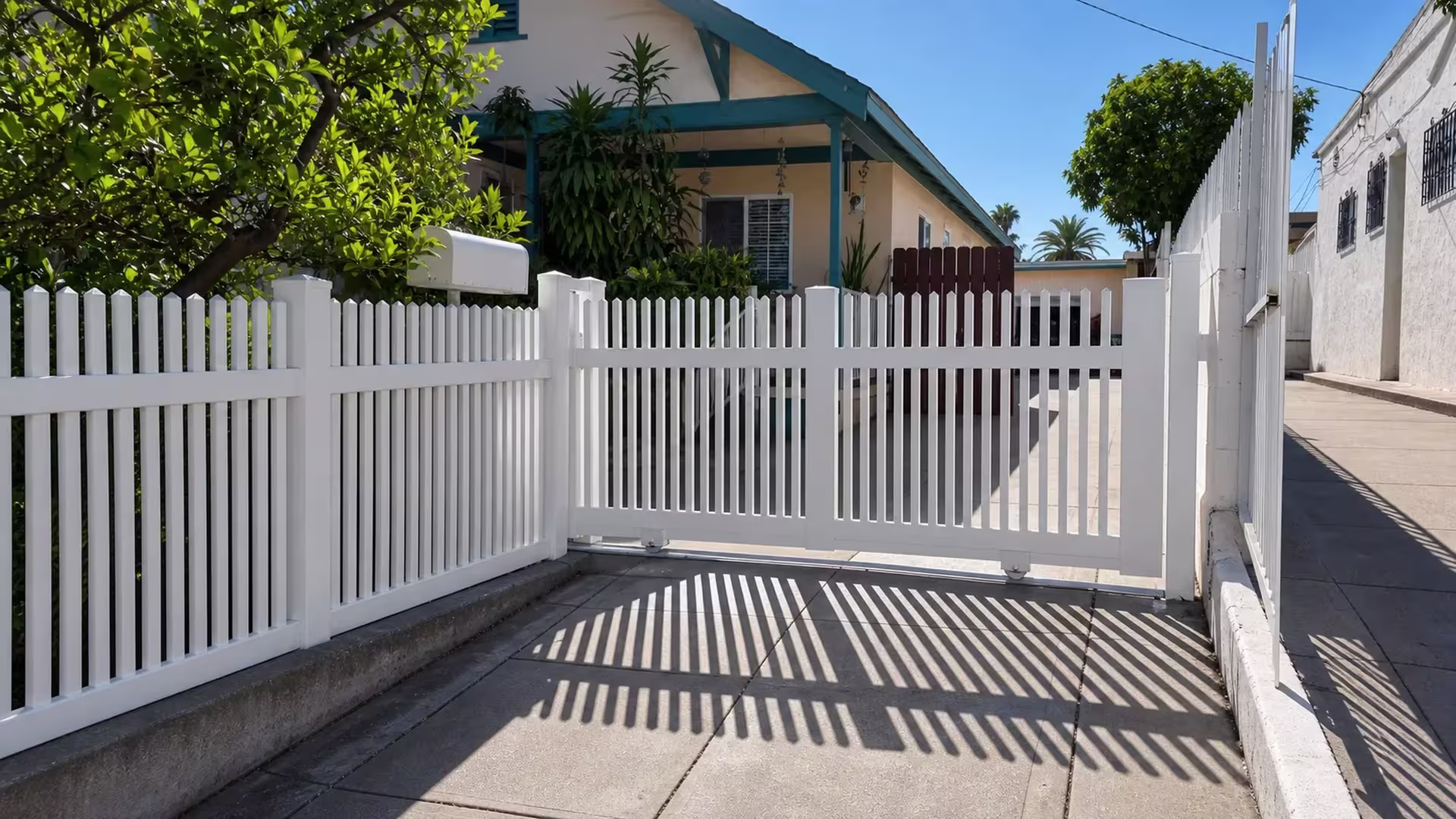White vinyl rolling picket gate split by a wide center stile into two bays of twenty-six pointed pickets on roller wheels