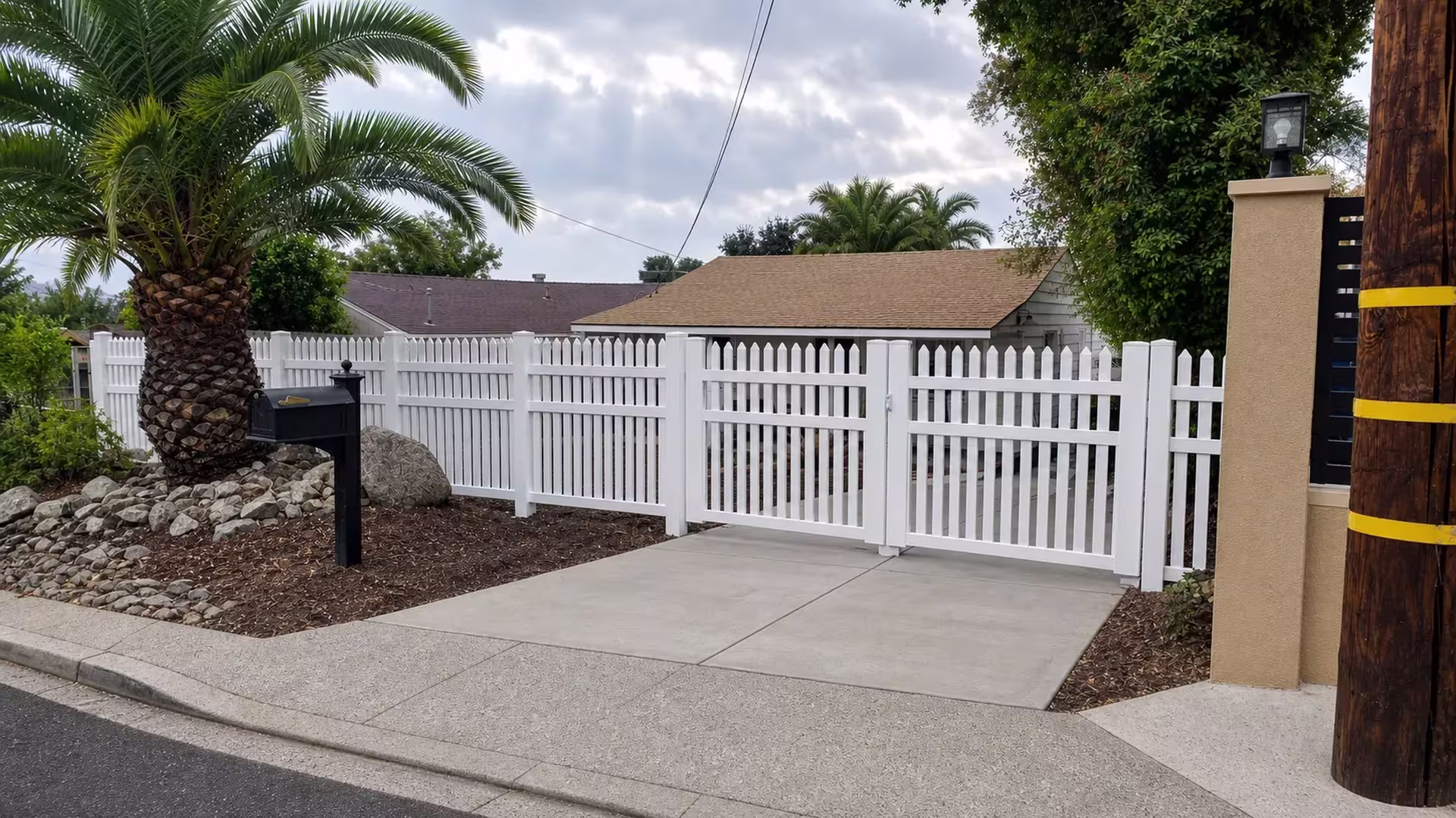 White vinyl two-leaf pointed-picket rolling gate meeting at a center latch beside a black side fence