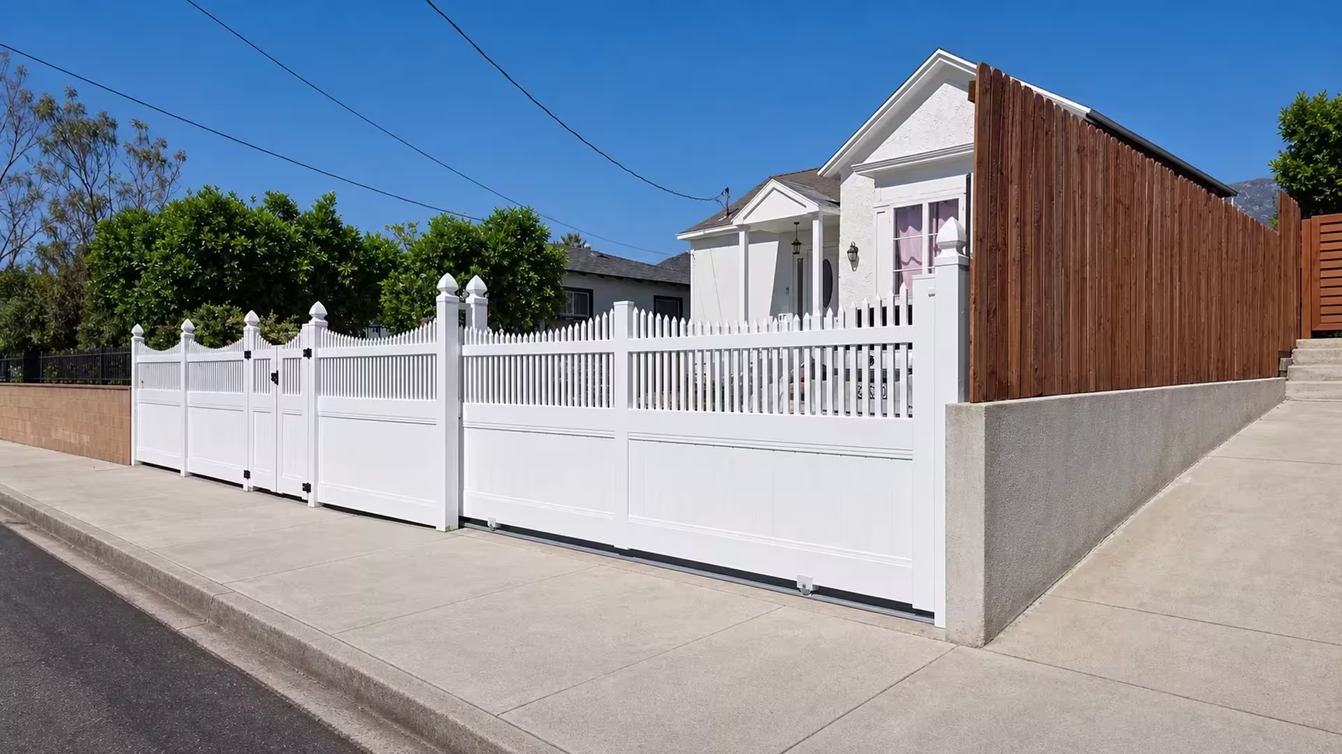 Capped end posts anchor this White vinyl privacy-picket rolling gate below a distant mountain peak