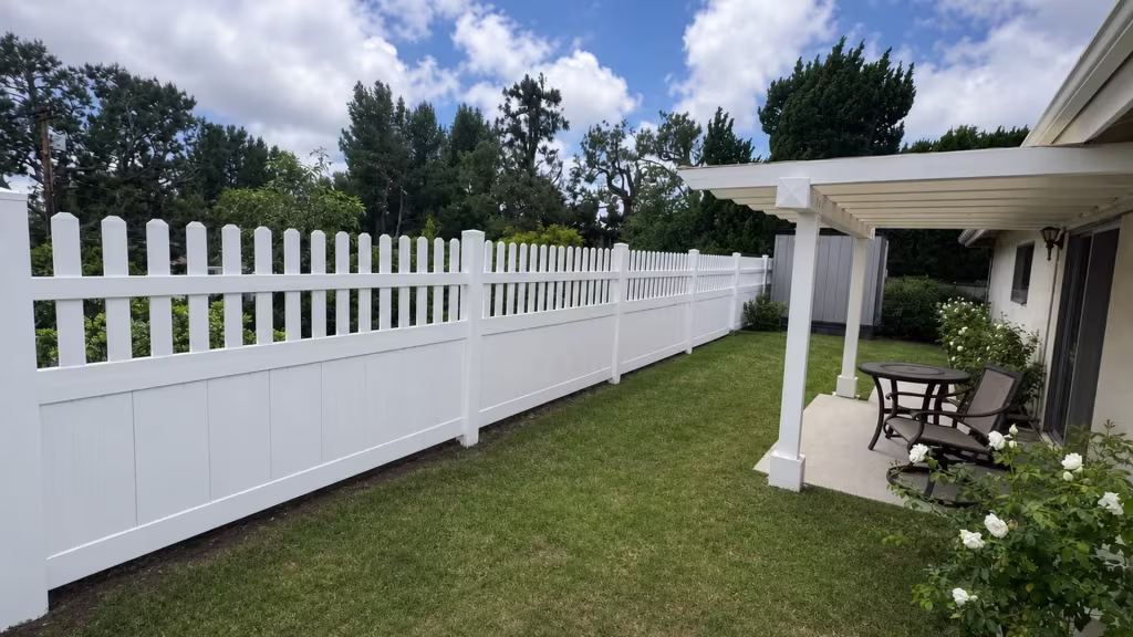 White vinyl picket-topped privacy fence continuing this rolling gate run near a patio cover and rose bushes