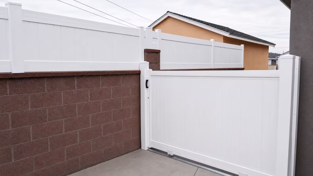 Black pull handle and roller brackets fit this White vinyl privacy rolling gate beside a pyramid-capped post