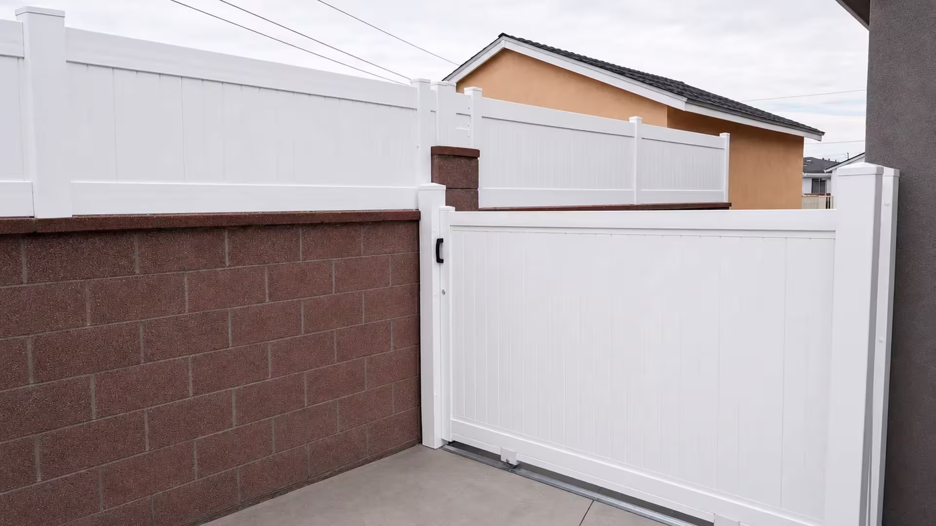 Black pull handle and roller brackets fit this White vinyl privacy rolling gate beside a pyramid-capped post