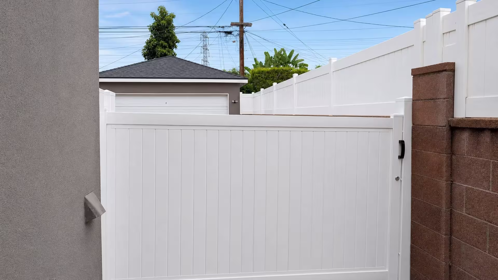 White vinyl solid-privacy rolling gate framed between a gray stucco wall and a capped brown masonry wall near a garage