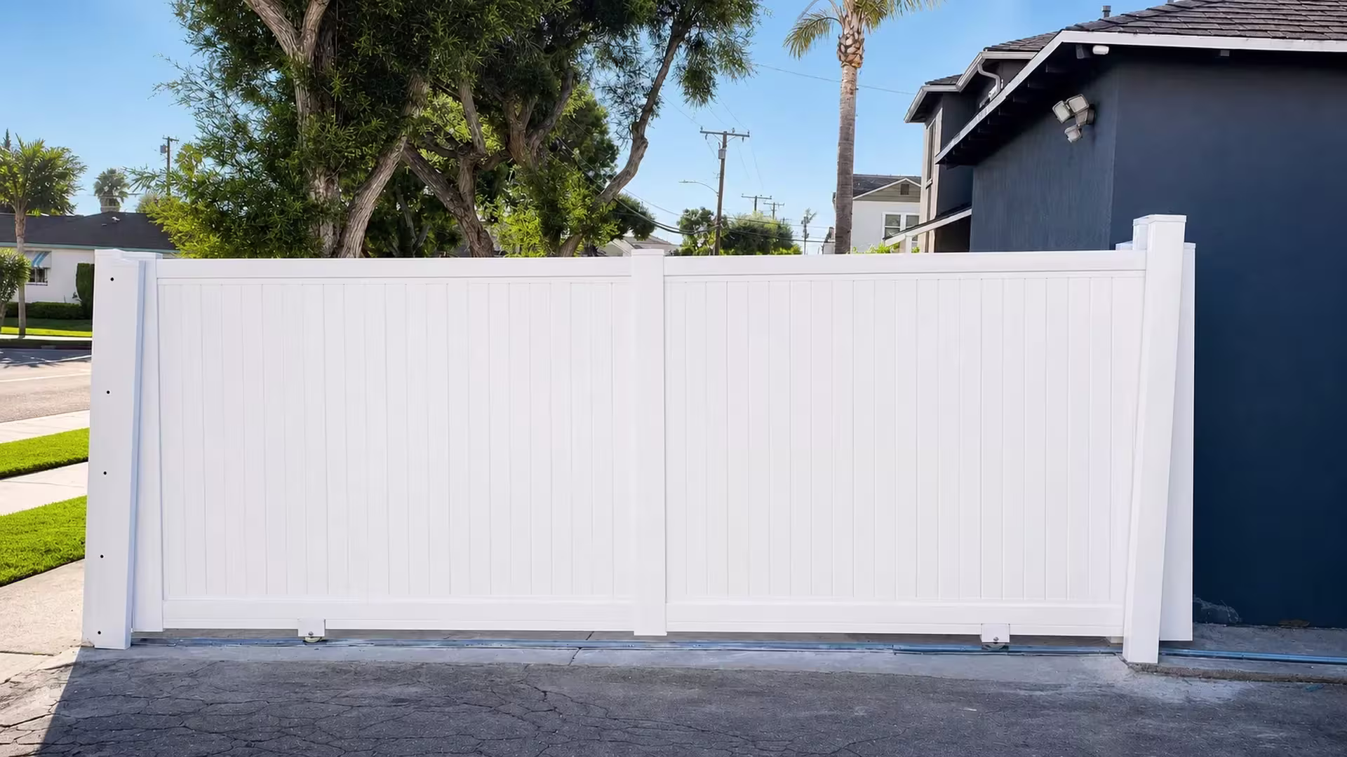 Dark blue house wall rises behind this White vinyl tongue-and-groove rolling gate split by a center stile