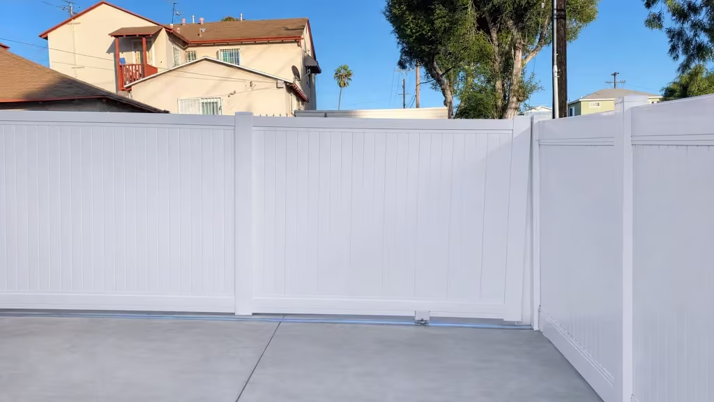 Open sky and neighboring rooflines frame this White vinyl solid rolling gate crossing the driveway opening