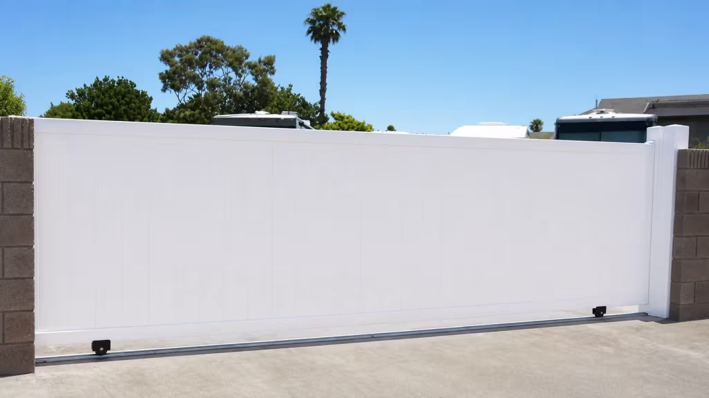 Two brown-gray masonry block columns anchor this wide-leaf White vinyl privacy rolling gate beneath a tall palm