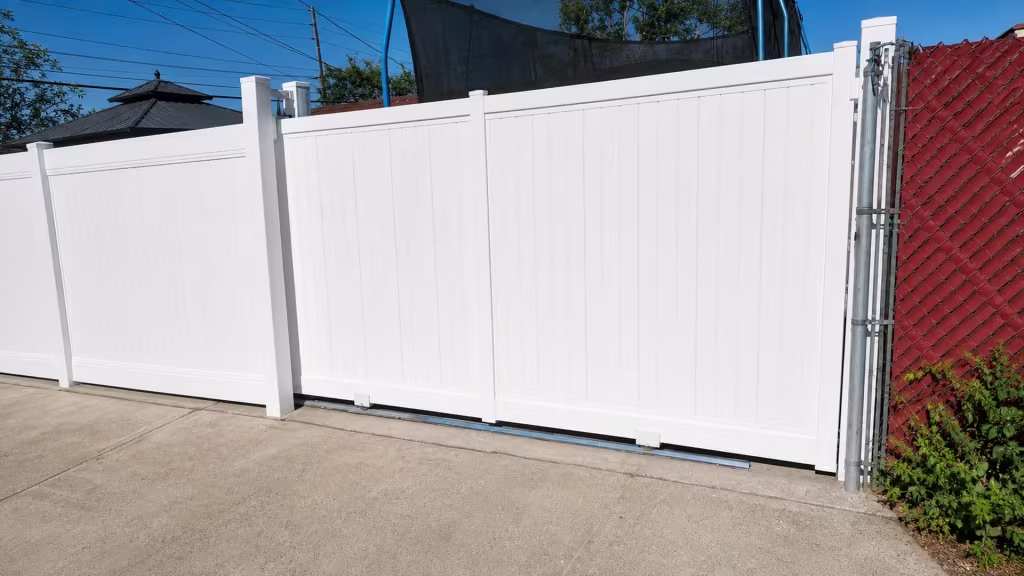 White vinyl privacy rolling gate sliding past a chain-link fence with red screening and climbing vines