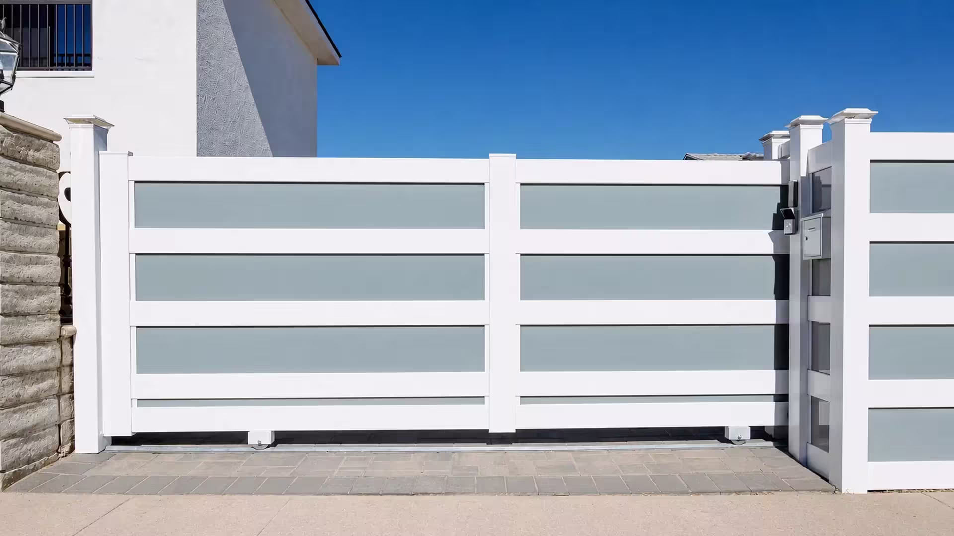 One wide White vinyl rolling gate leaf on a ground track, split by a center stile in front of a stucco house