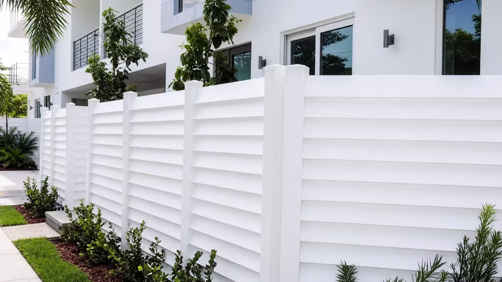 This horizontal-louver semi-privacy fence in White vinyl runs the length of a multi-story residence wall