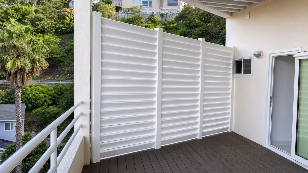Elevated hillside deck wrapped in a Cream vinyl louvered semi-privacy fence beside the stucco house wall