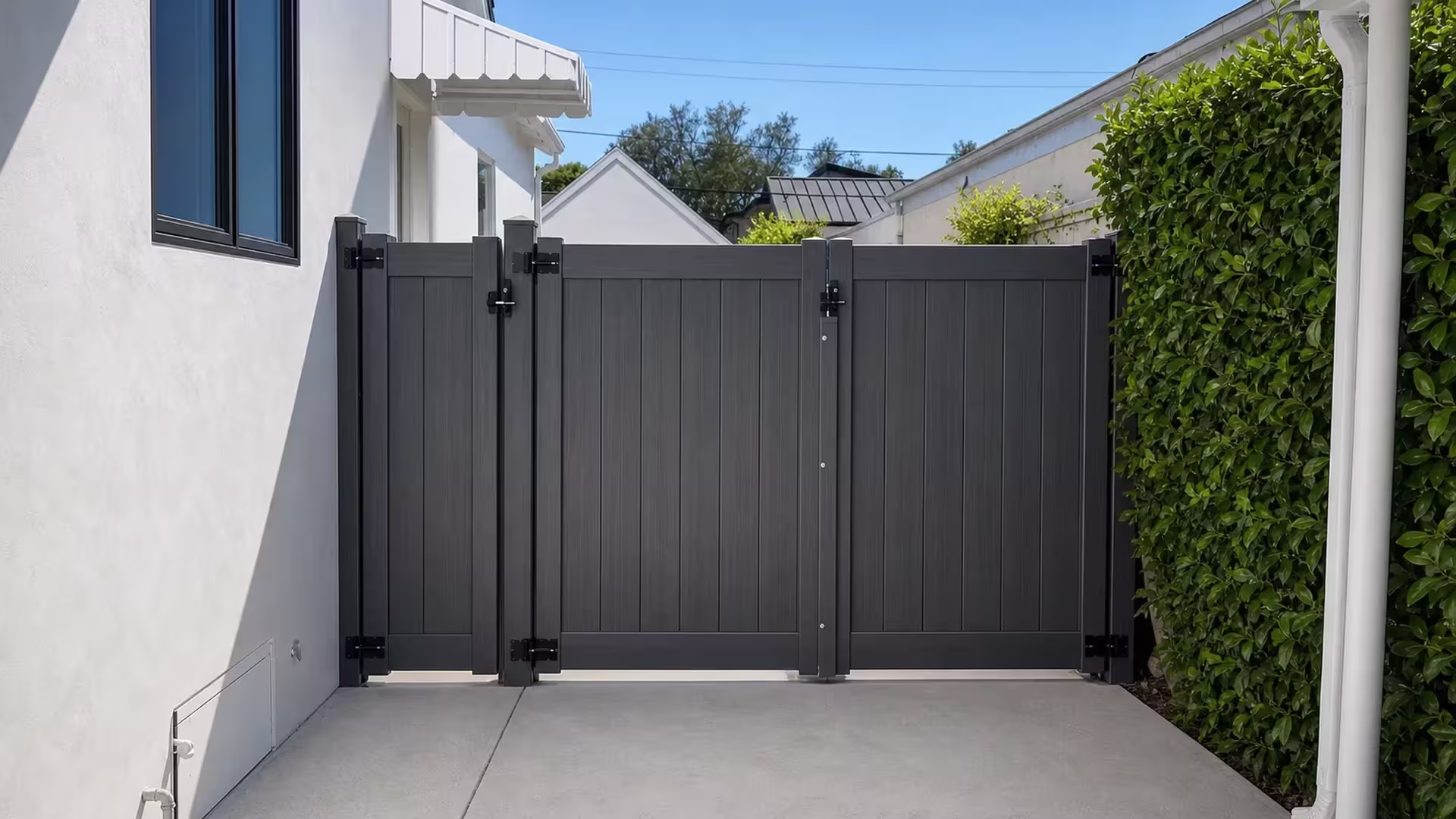 Arctic Blend vinyl side gate spanning a driveway between a white stucco house and a dense hedge