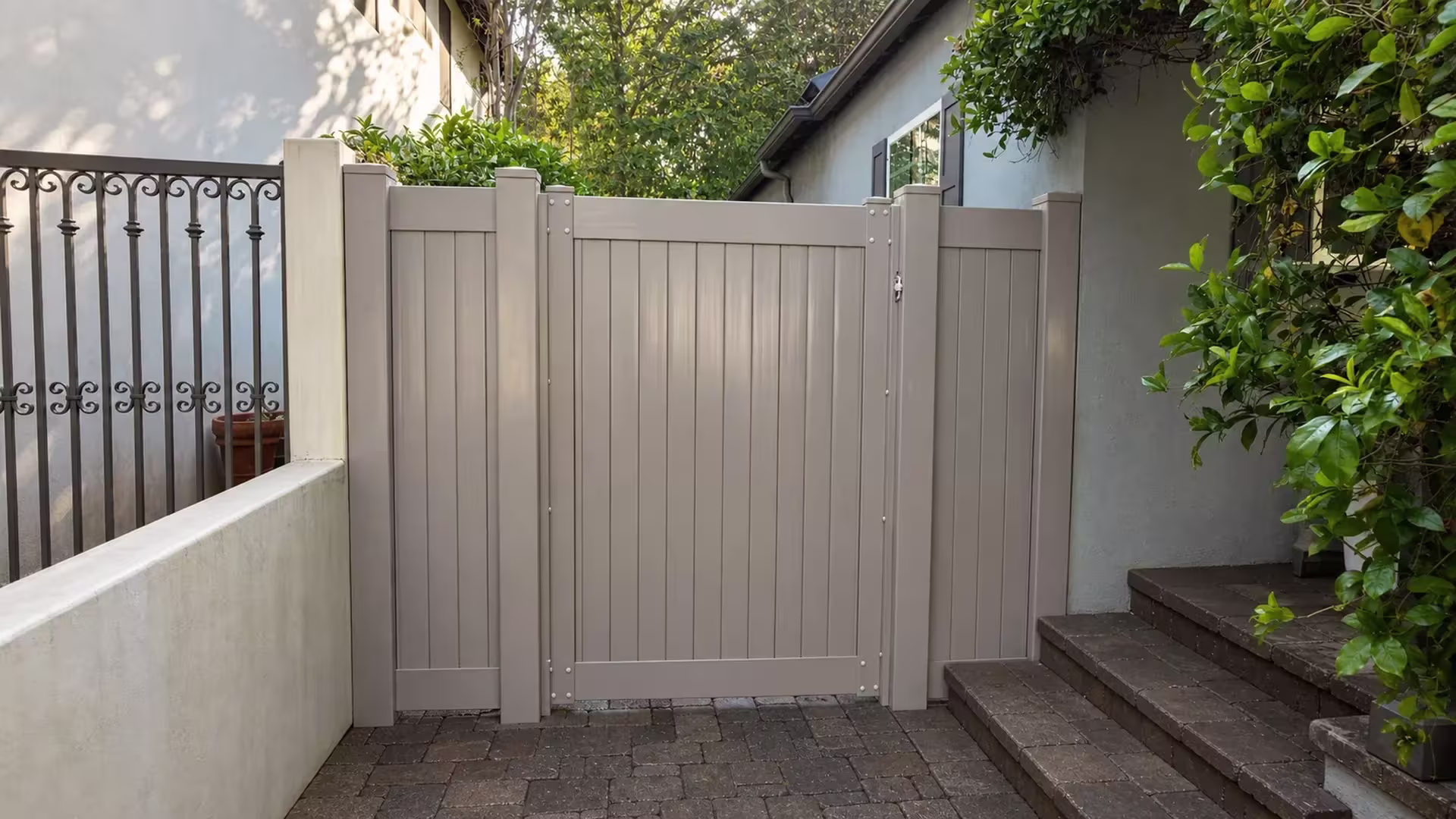 Clay vinyl side gate spanning a paved courtyard beside a low masonry wall and iron railing