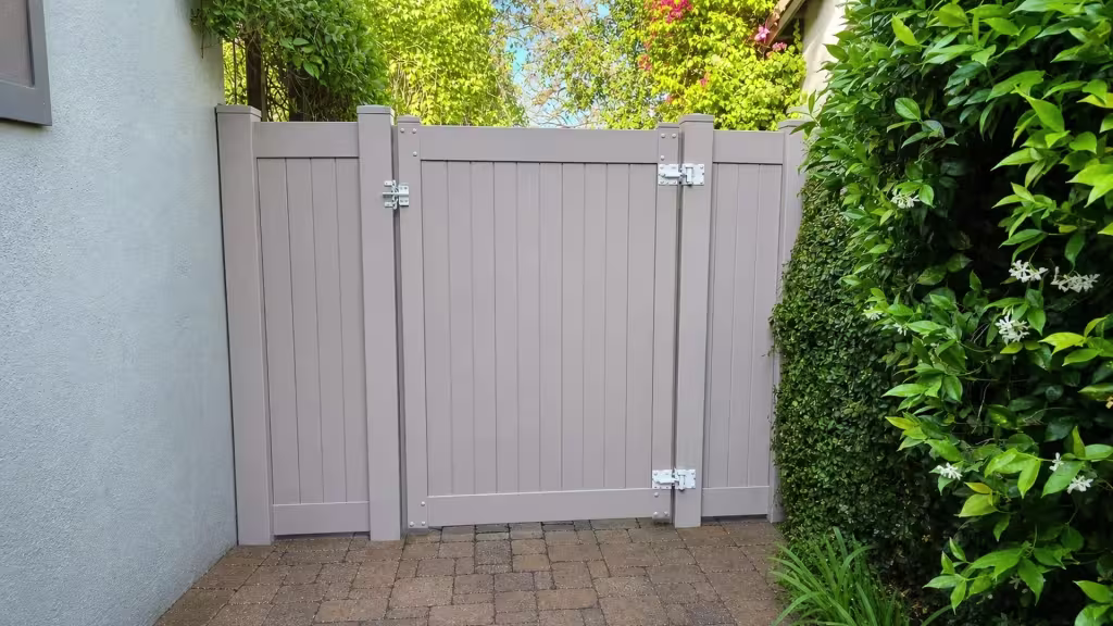 Clay vinyl side gate closing a narrow paved side yard bordered by dense hedges