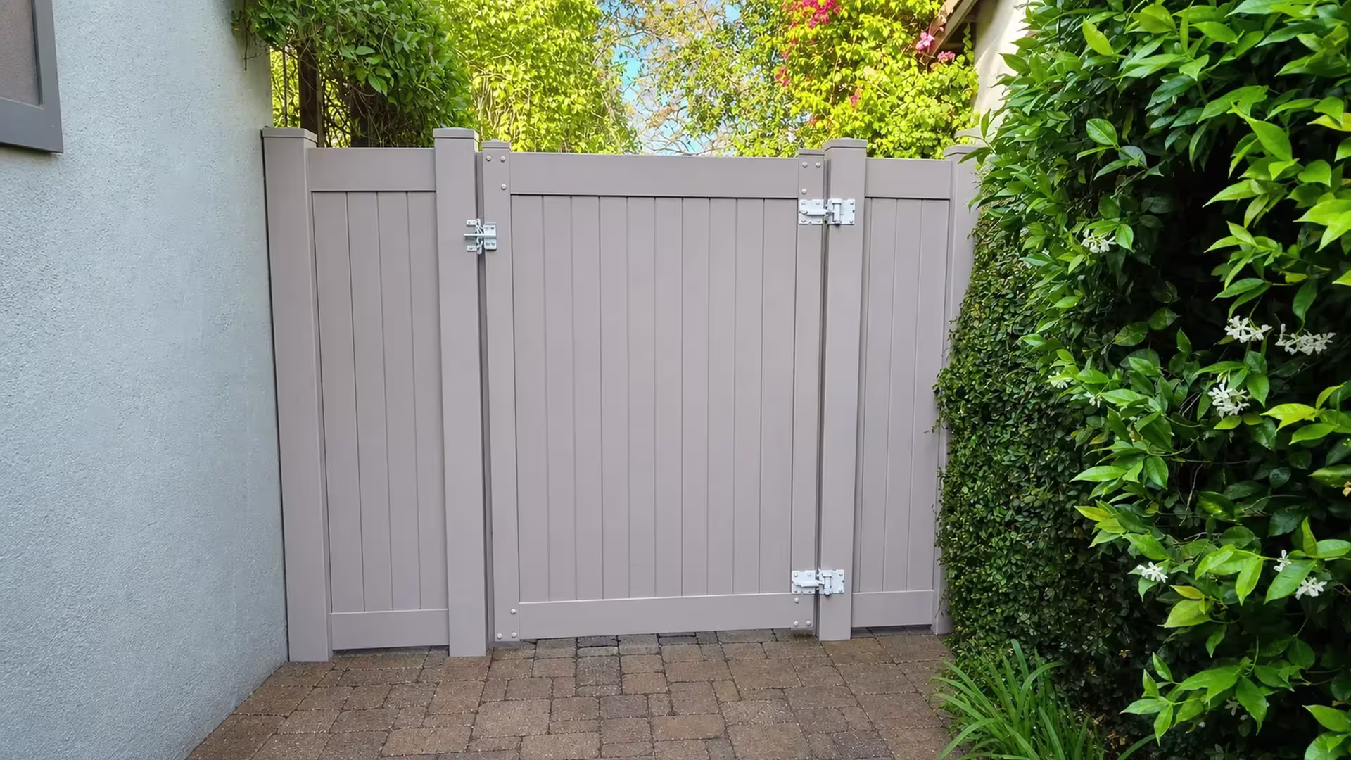 Clay vinyl side gate closing a narrow paved side yard bordered by dense hedges