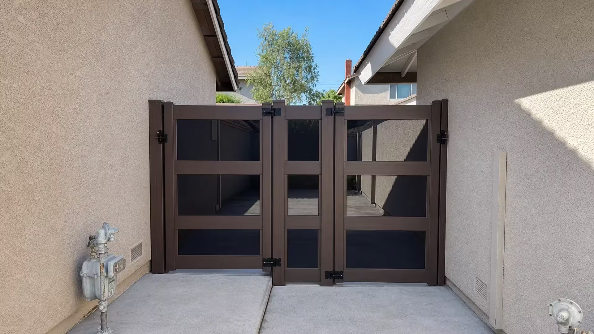 Three square capped posts carry a Dark Walnut vinyl gate assembly along a concrete passage