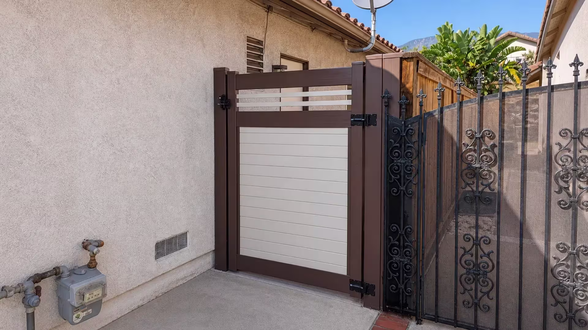 Dark Walnut vinyl side gate closing the gap between a stucco house and a scroll pattern metal fence