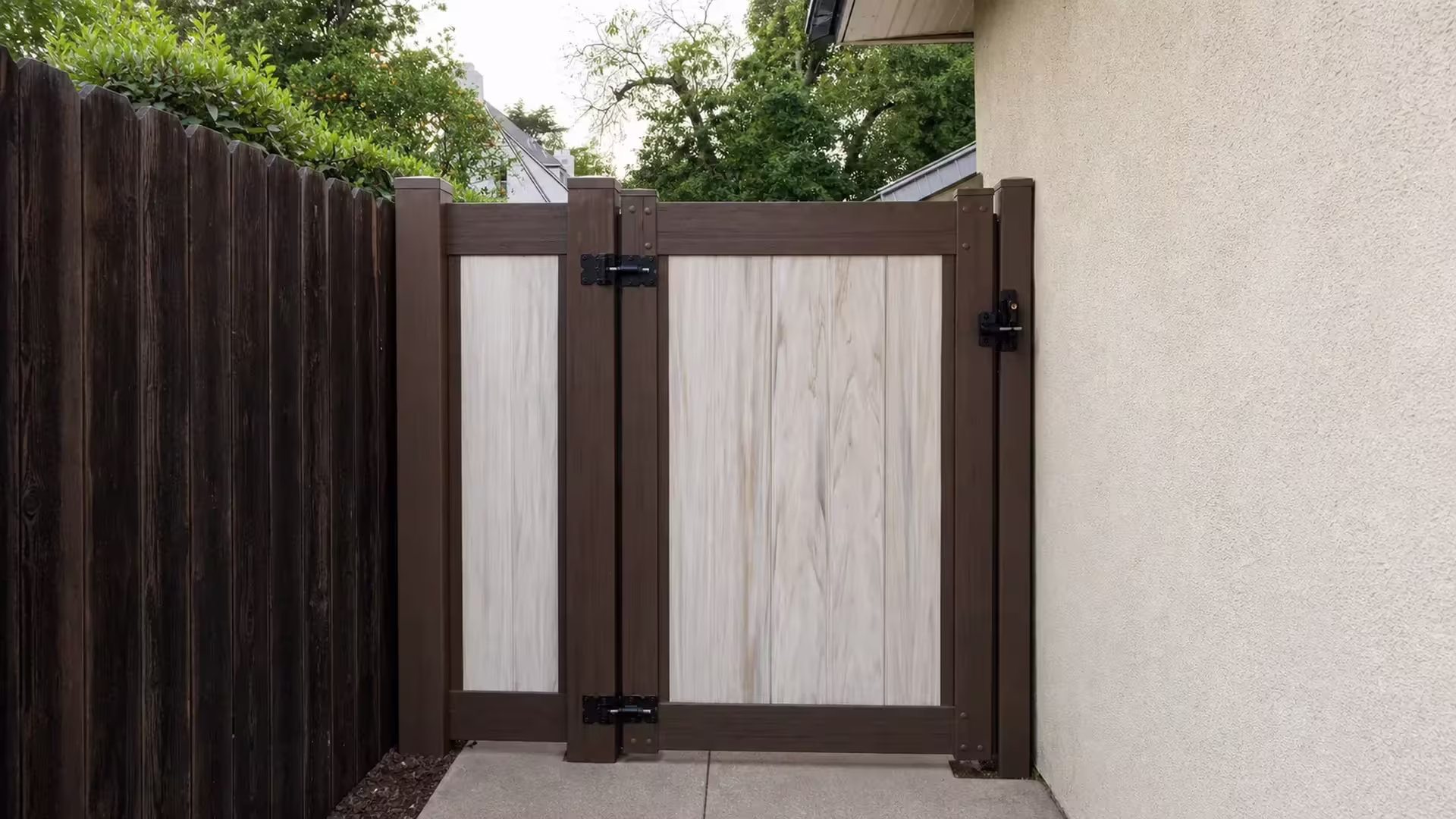An existing wood fence meets a Dark Walnut vinyl side gate beside the beige stucco house wall