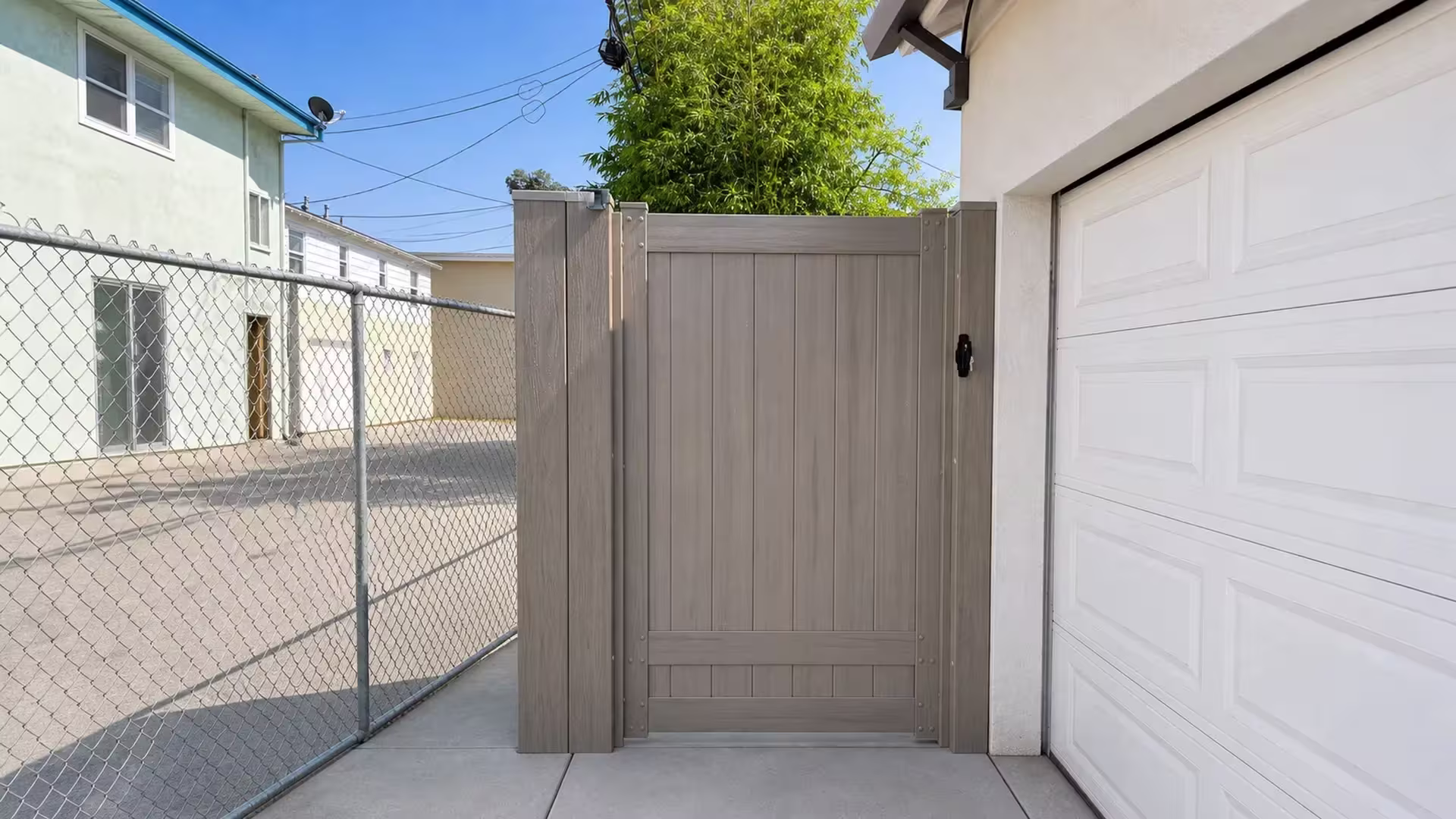 Mesquite vinyl side gate standing beside the white stucco garage wall and a chain-link boundary fence