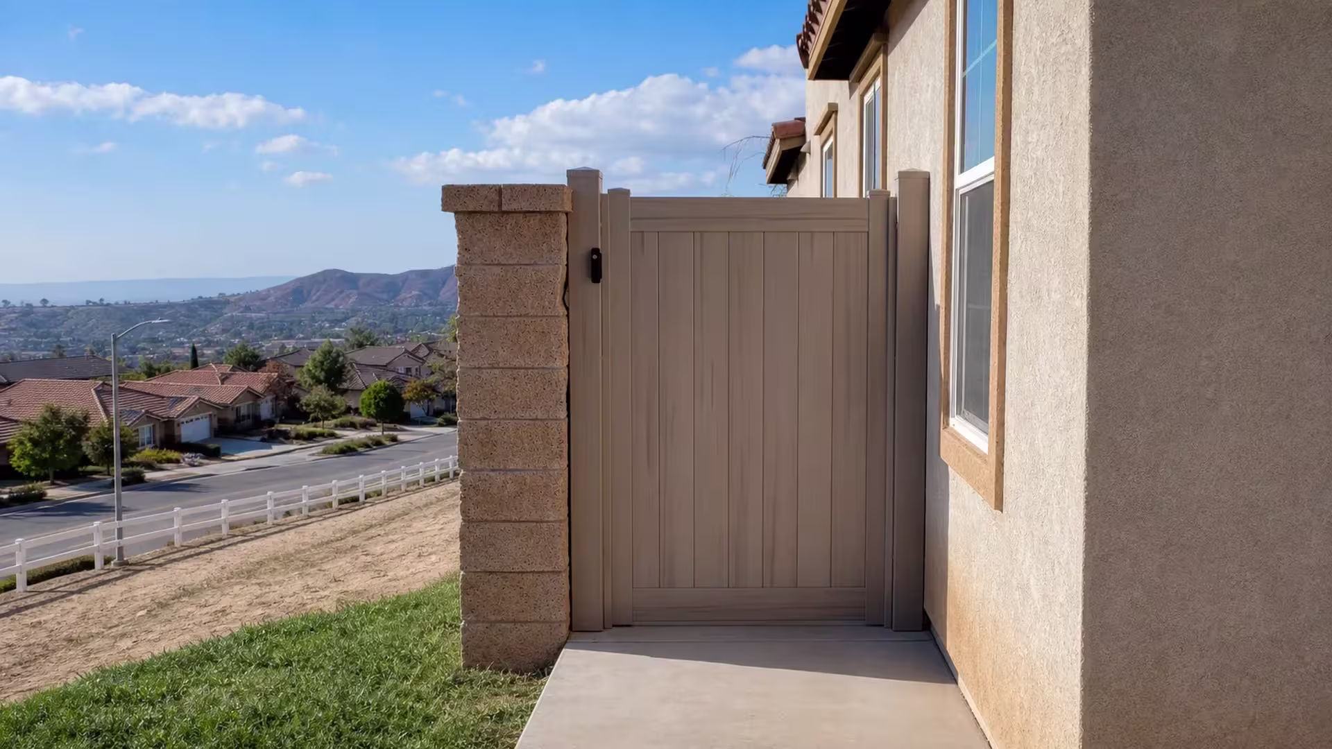 Mesquite vinyl side gate crossing a concrete walkway with a distant mountain rising behind the hillside homes