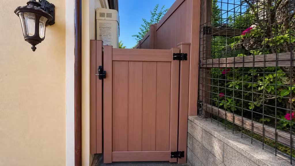 Sierra Blend vinyl side gate standing next to a dark metal garden trellis and a vertical drainpipe
