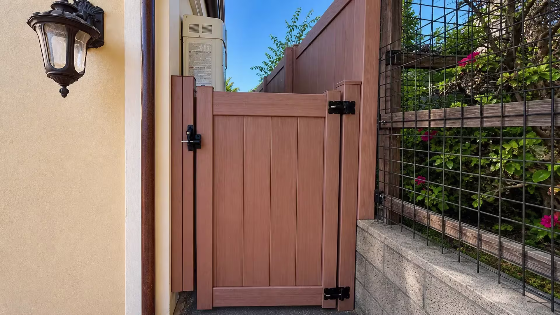 Sierra Blend vinyl side gate standing next to a dark metal garden trellis and a vertical drainpipe