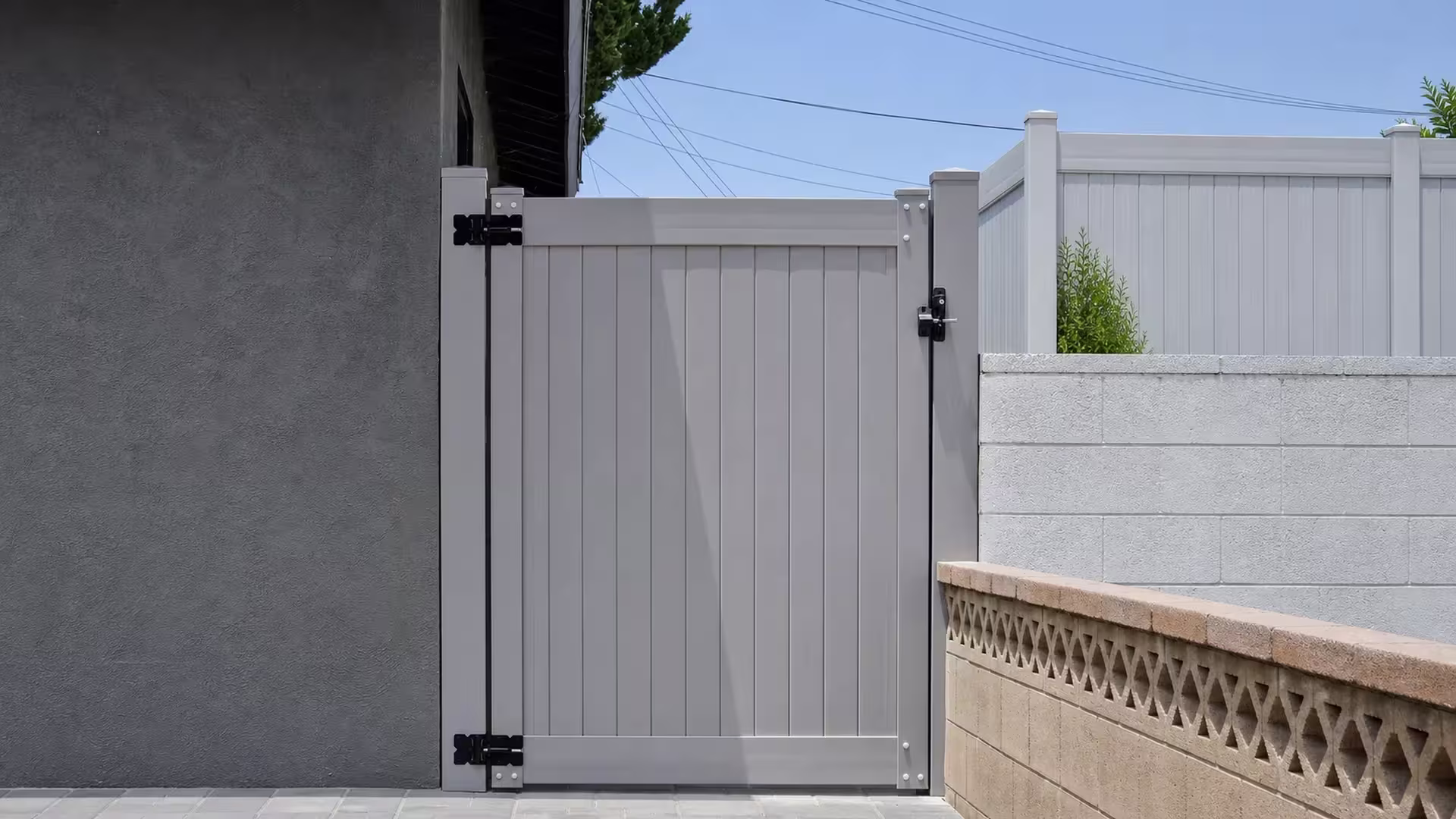 Slate Gray vinyl side gate spanning the gap between a dark stucco building and concrete-block walls