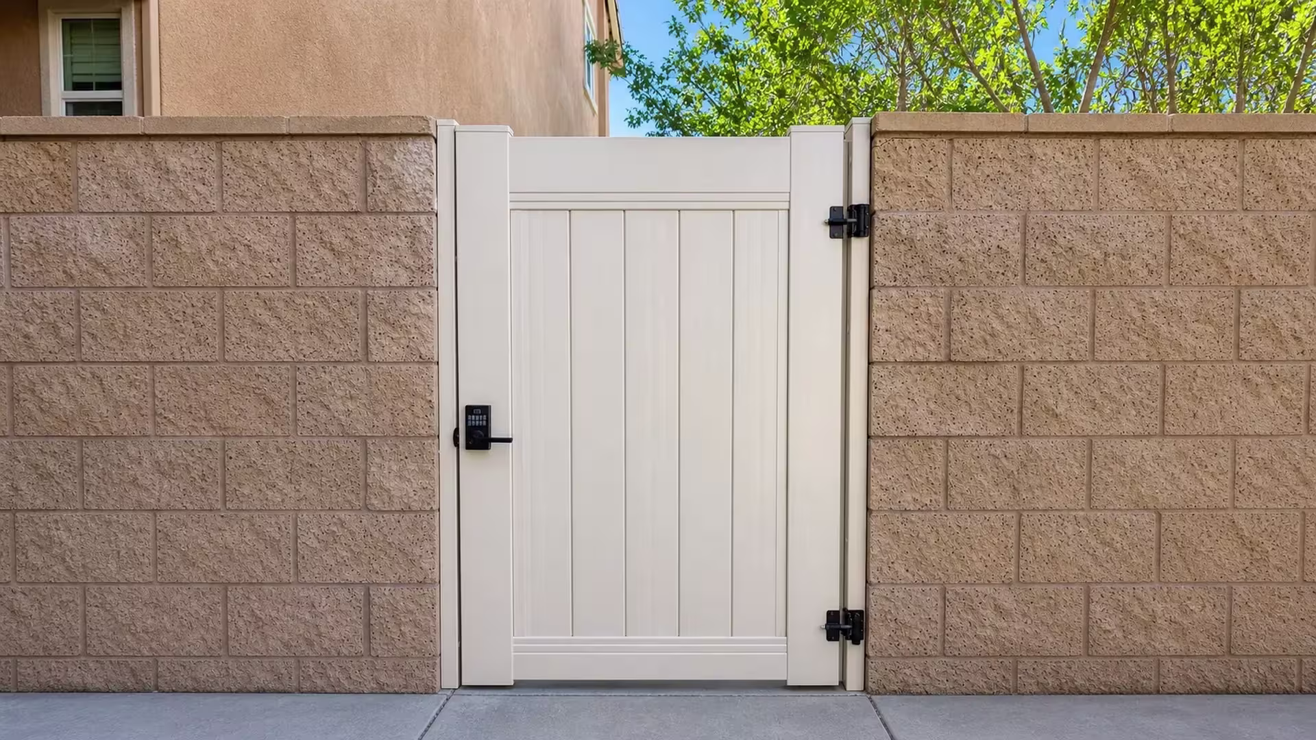 Tan vinyl side gate fitted between matching split-face block piers with a window glimpsed behind