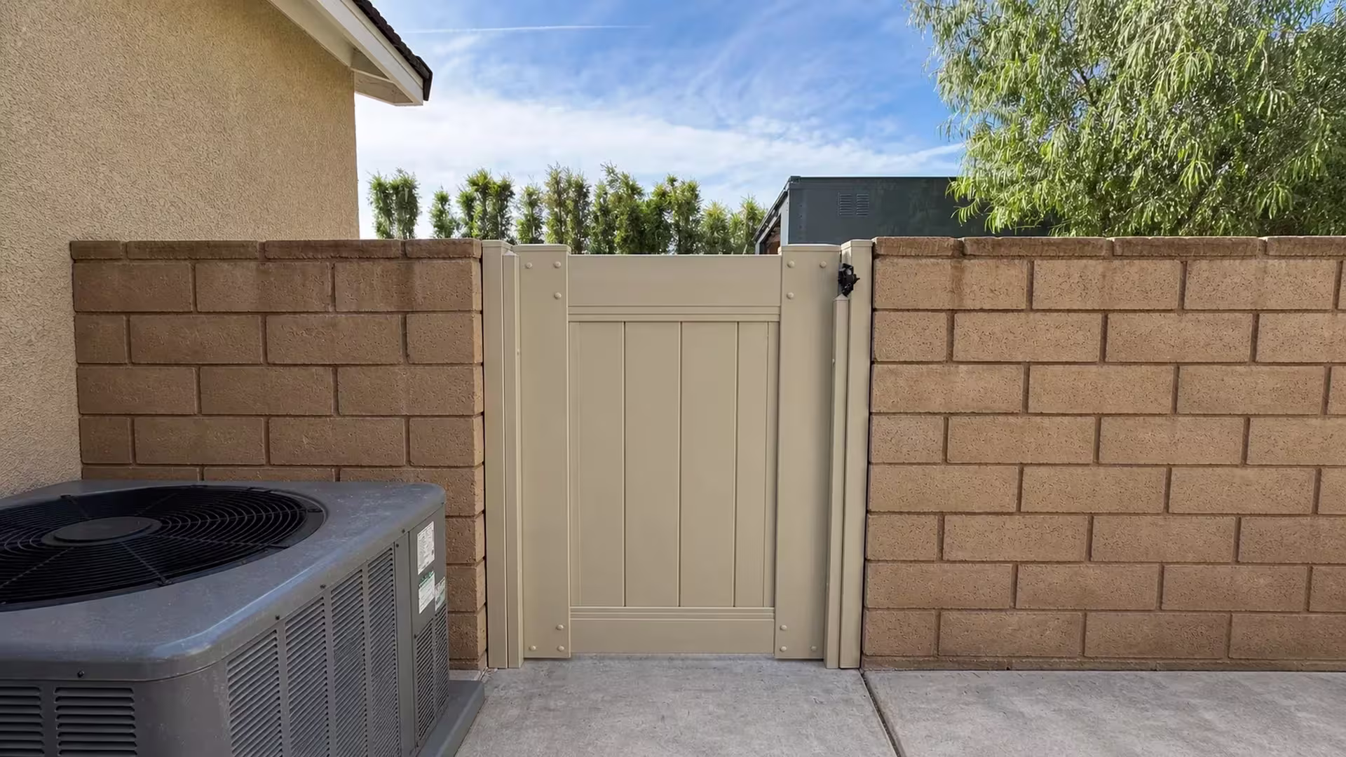 Tan vinyl side gate installed beside masonry walls with an HVAC condenser unit at the lower left
