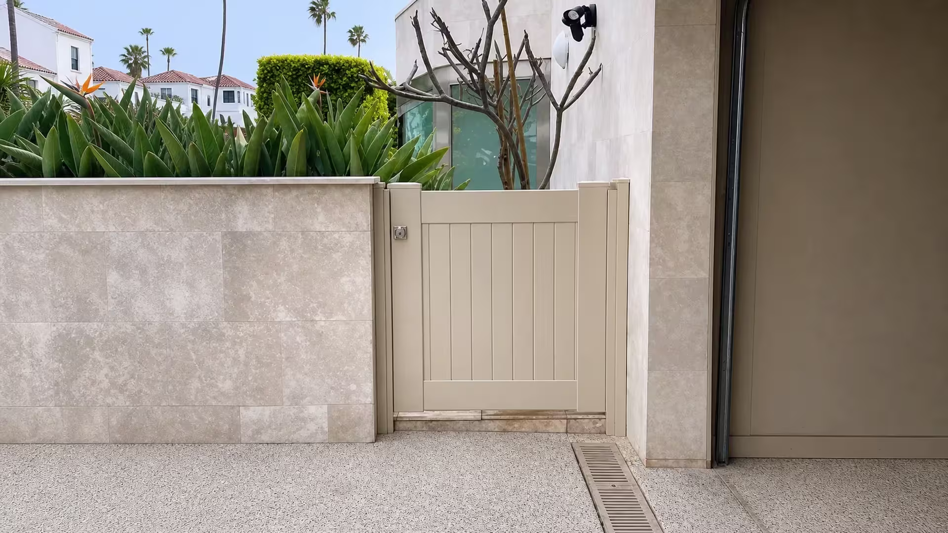 Pebble-textured paving and a drainage channel lead to this Tan vinyl side gate in the stucco opening