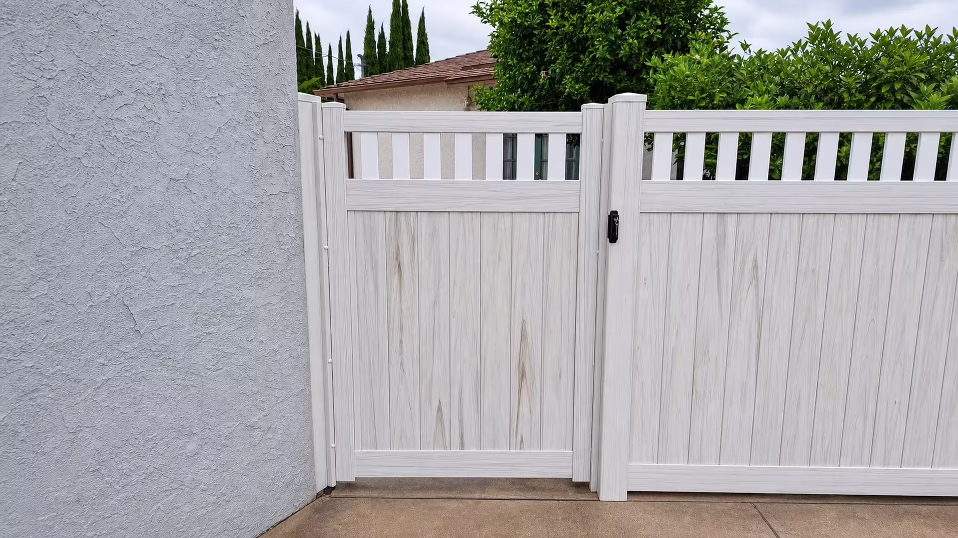 Weathered Aspen vinyl side gate closing a passage lined with cypress and a citrus tree