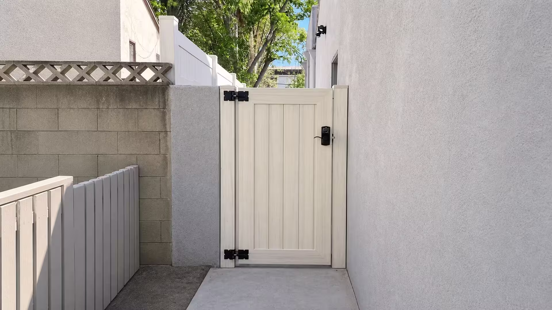 Weathered Aspen vinyl side gate spanning the passage between a gray masonry boundary and a white stucco building