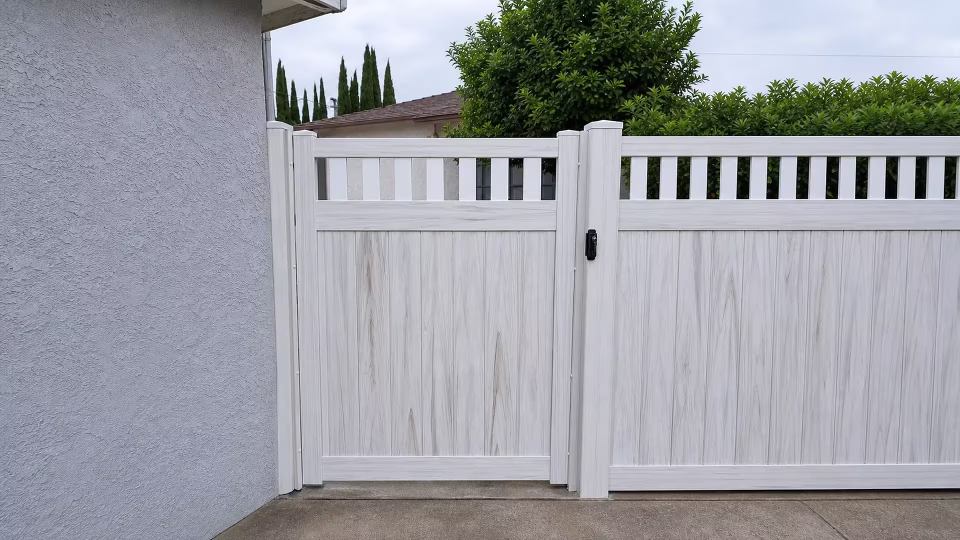 Weathered Aspen vinyl side gate framed by columnar evergreens beside a neighboring tiled roofline