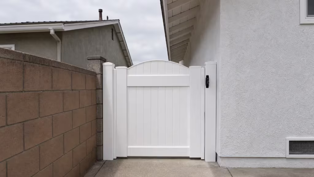 Arched White vinyl side gate closes a narrow residential passage beside a block wall