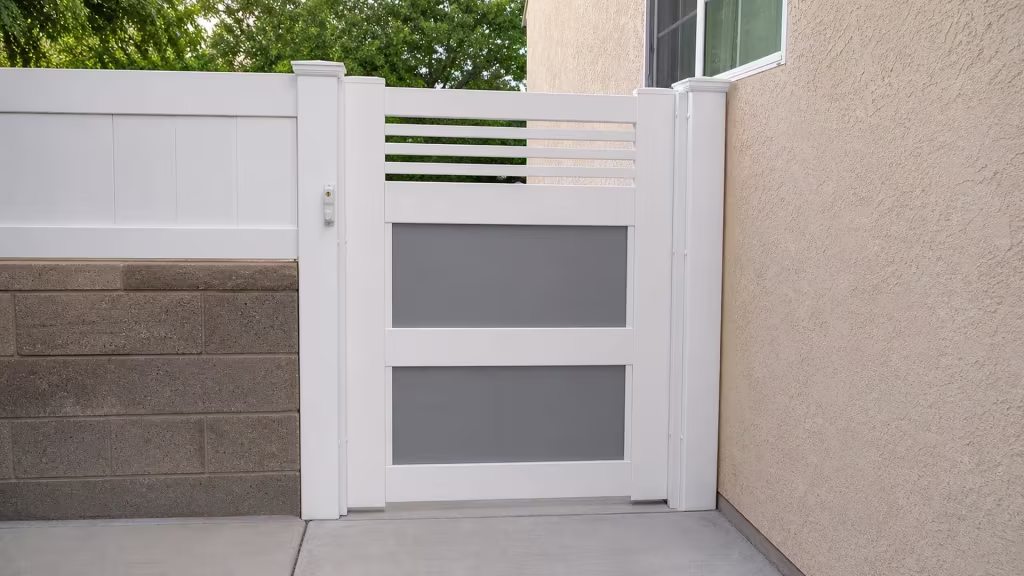 White vinyl side gate stands between two posts beside a stucco house wall and concrete threshold