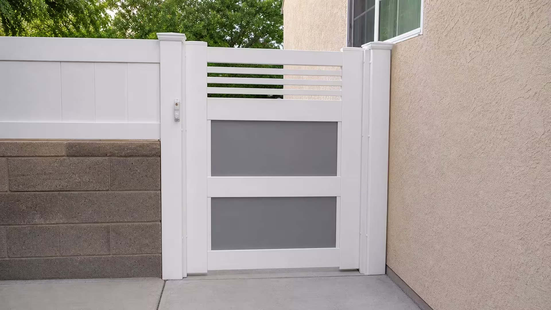 White vinyl side gate stands between two posts beside a stucco house wall and concrete threshold