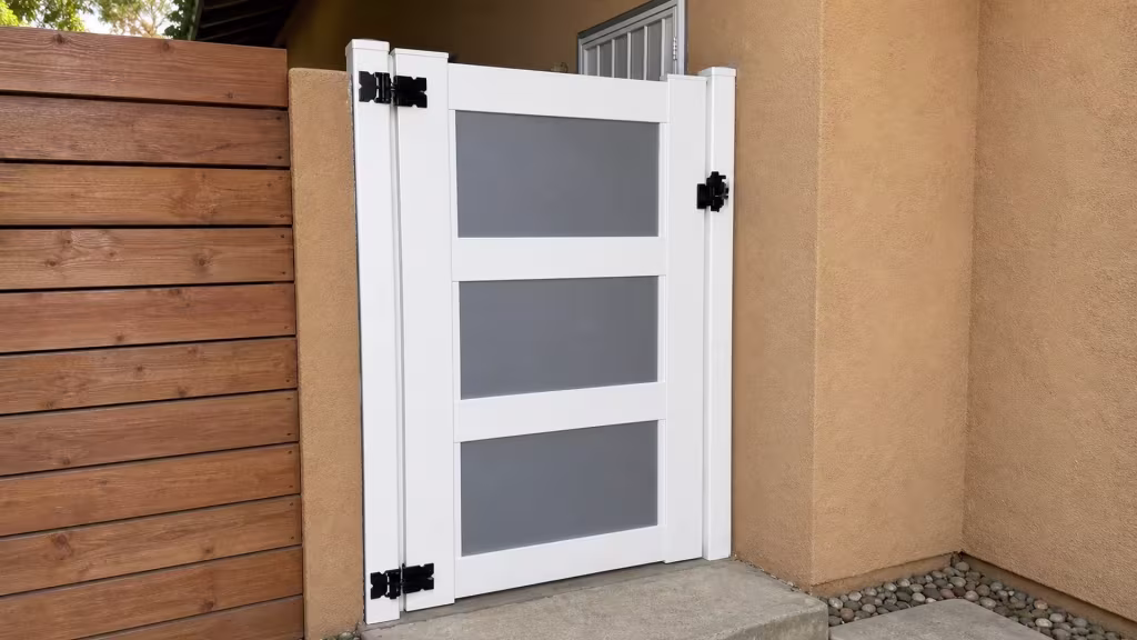A river rock drainage strip runs below this White vinyl side gate fitted between stucco walls