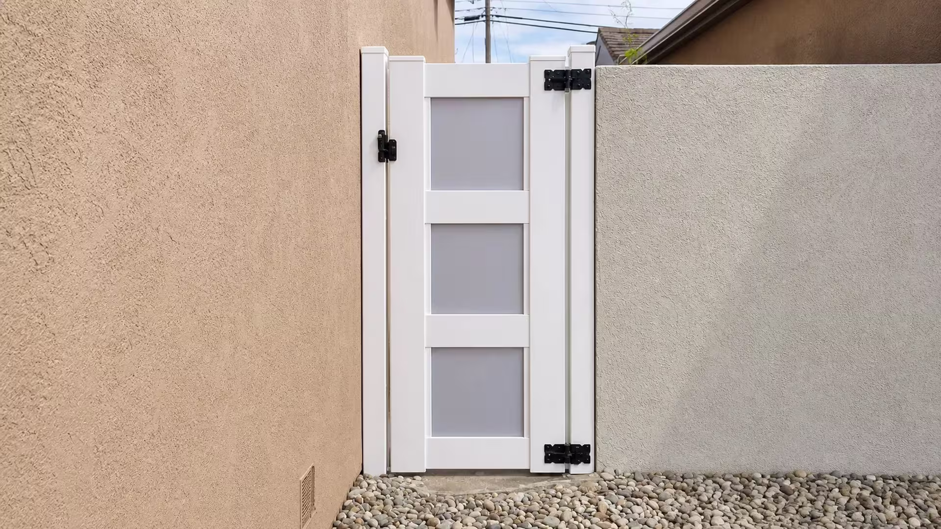 Overhead utility lines cross above this White vinyl side gate wedged tightly between two stucco walls