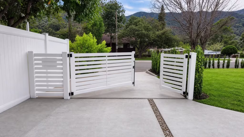 White vinyl side gate closing a driveway opening with a distant mountain rising above the street
