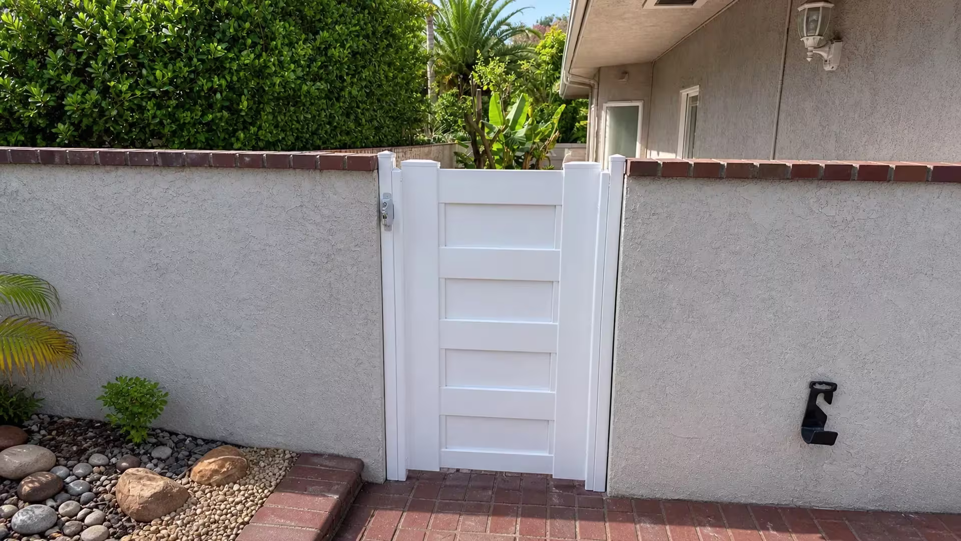 Reddish brown coping bricks top the stucco walls flanking this White vinyl side gate
