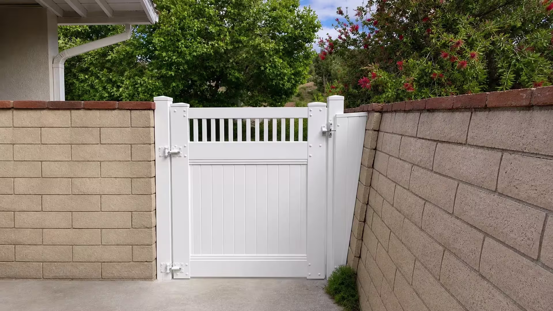 Concrete block walls frame this White vinyl side gate near a flowering bottlebrush shrub