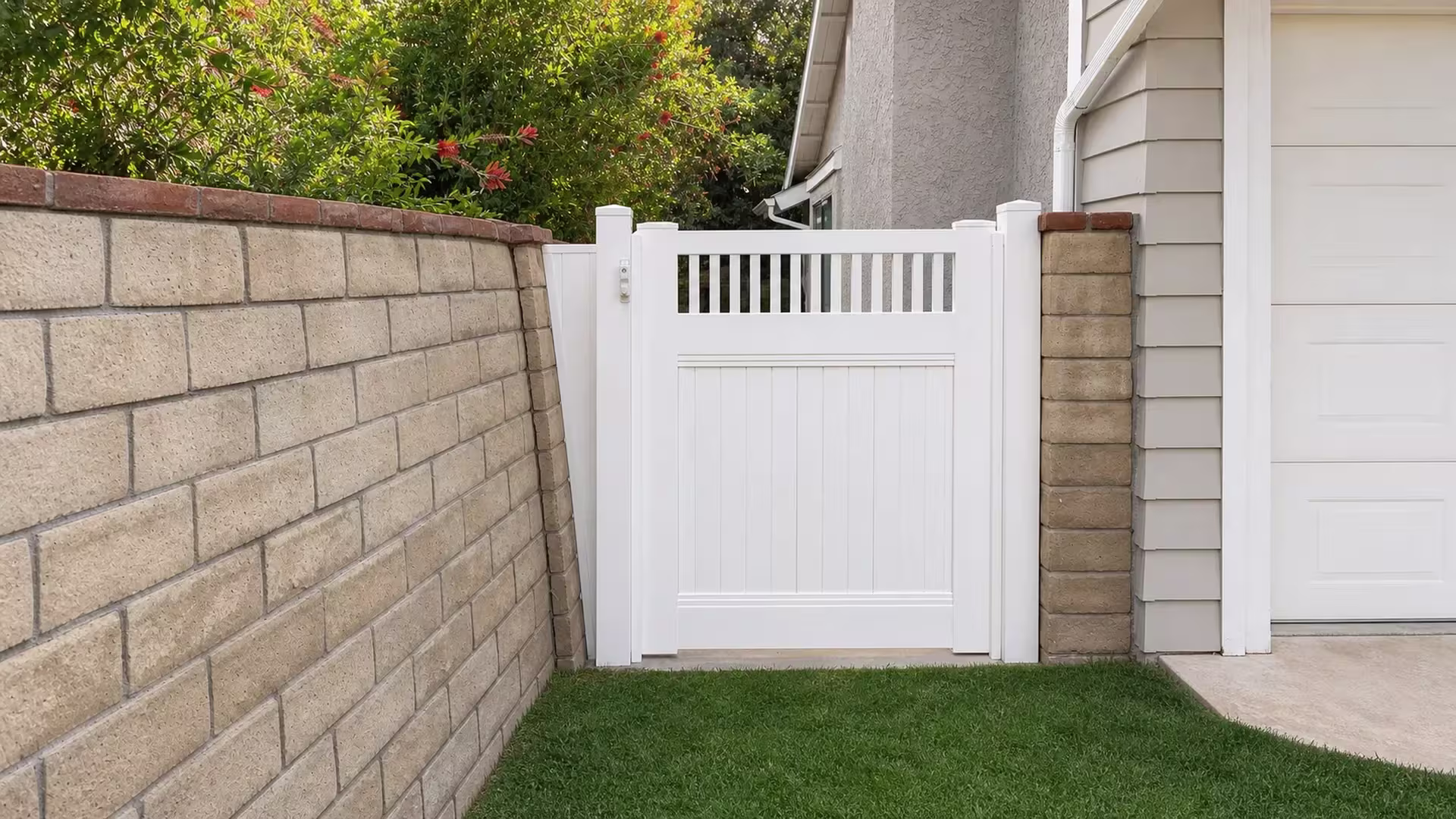 A masonry garden wall meets this White vinyl side gate closing a passage beside a house pillar