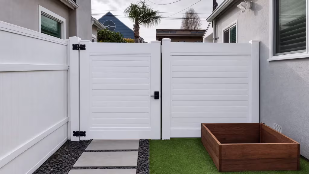 A wider fixed panel sits beside this White vinyl side gate, its horizontal boards running past a utility pole and palm