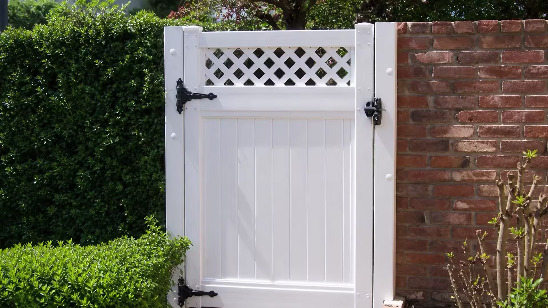 A red brick pier flanks this White vinyl side gate, framed by two square posts beside dense garden planting