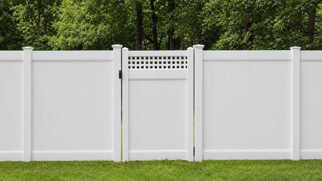 A matching privacy fence line centers this White vinyl side gate, facing an open lawn and a wooded backdrop