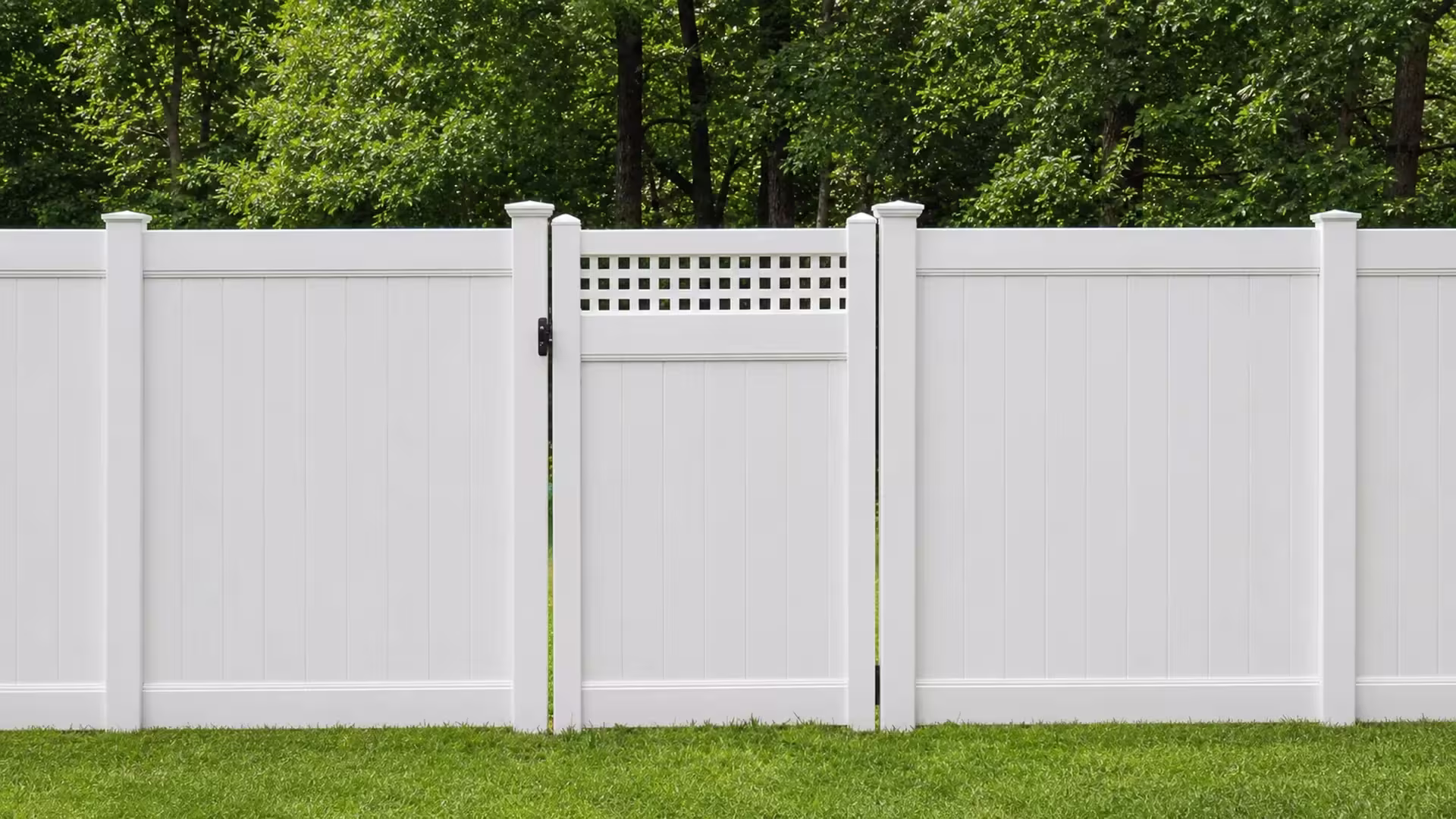 A matching privacy fence line centers this White vinyl side gate, facing an open lawn and a wooded backdrop