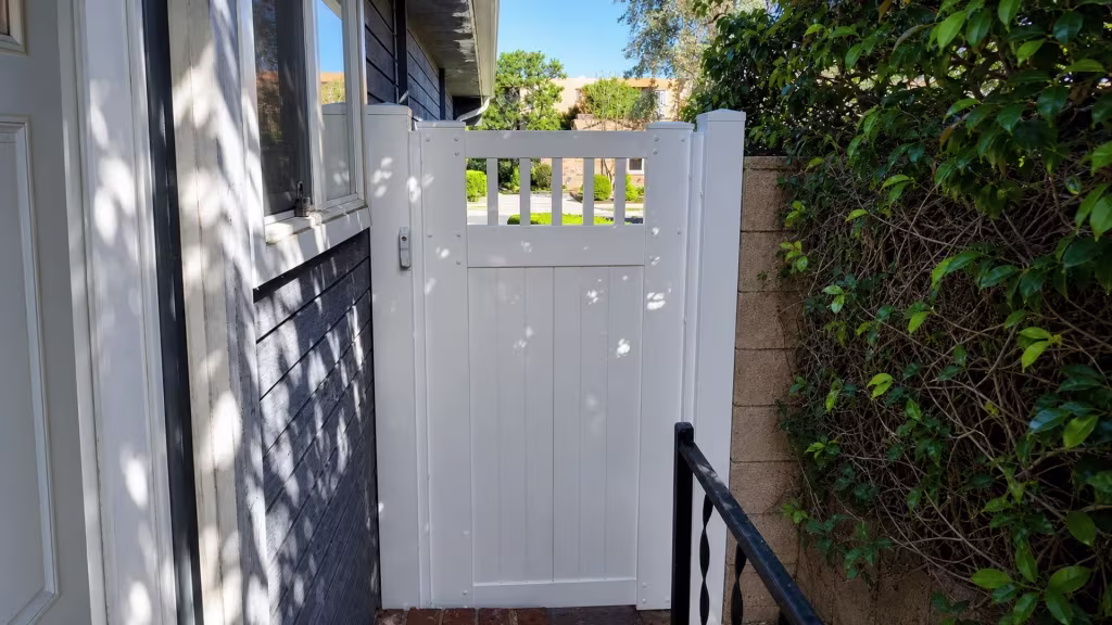 Open picket bays top this White vinyl side gate above solid boards, beside a black metal handrail and brick step
