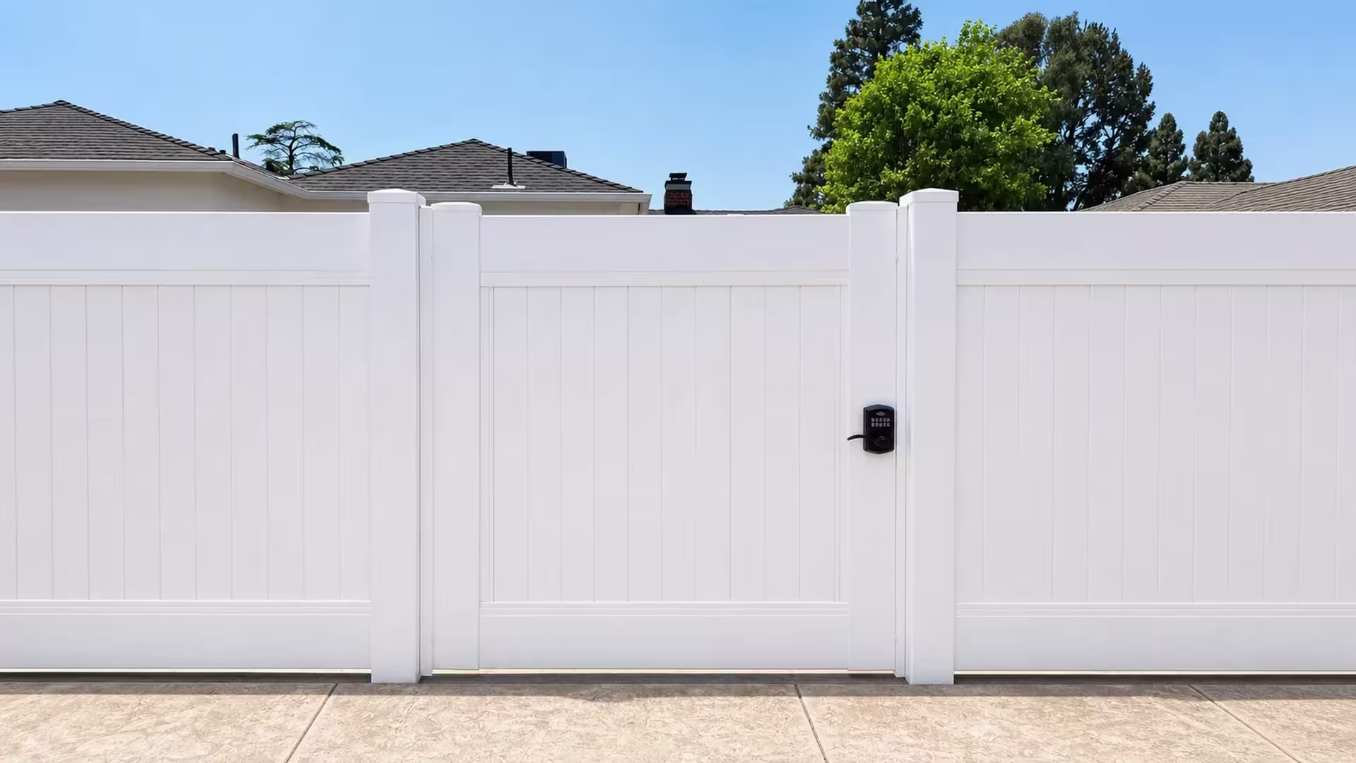 Rooftops and a chimney rise behind this White vinyl side gate centered in a privacy fence run, with paved ground below